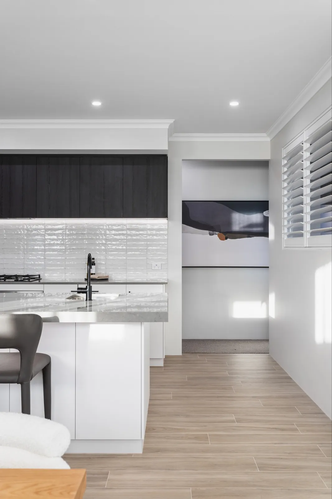 Kitchen island with a white tile splashback and dark cabinetry opening onto a hallway with timber-look floor tiles